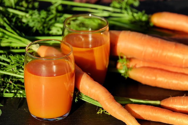 Carote con radice e un bicchiere di succo di carota.